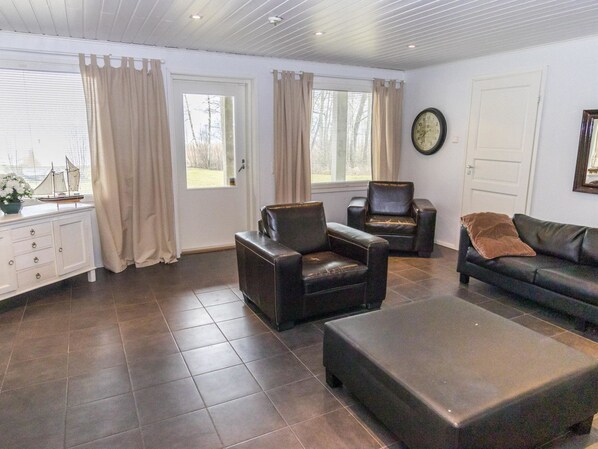 A spacious living room with a large window, a sofa, two armchairs, and a coffee table.