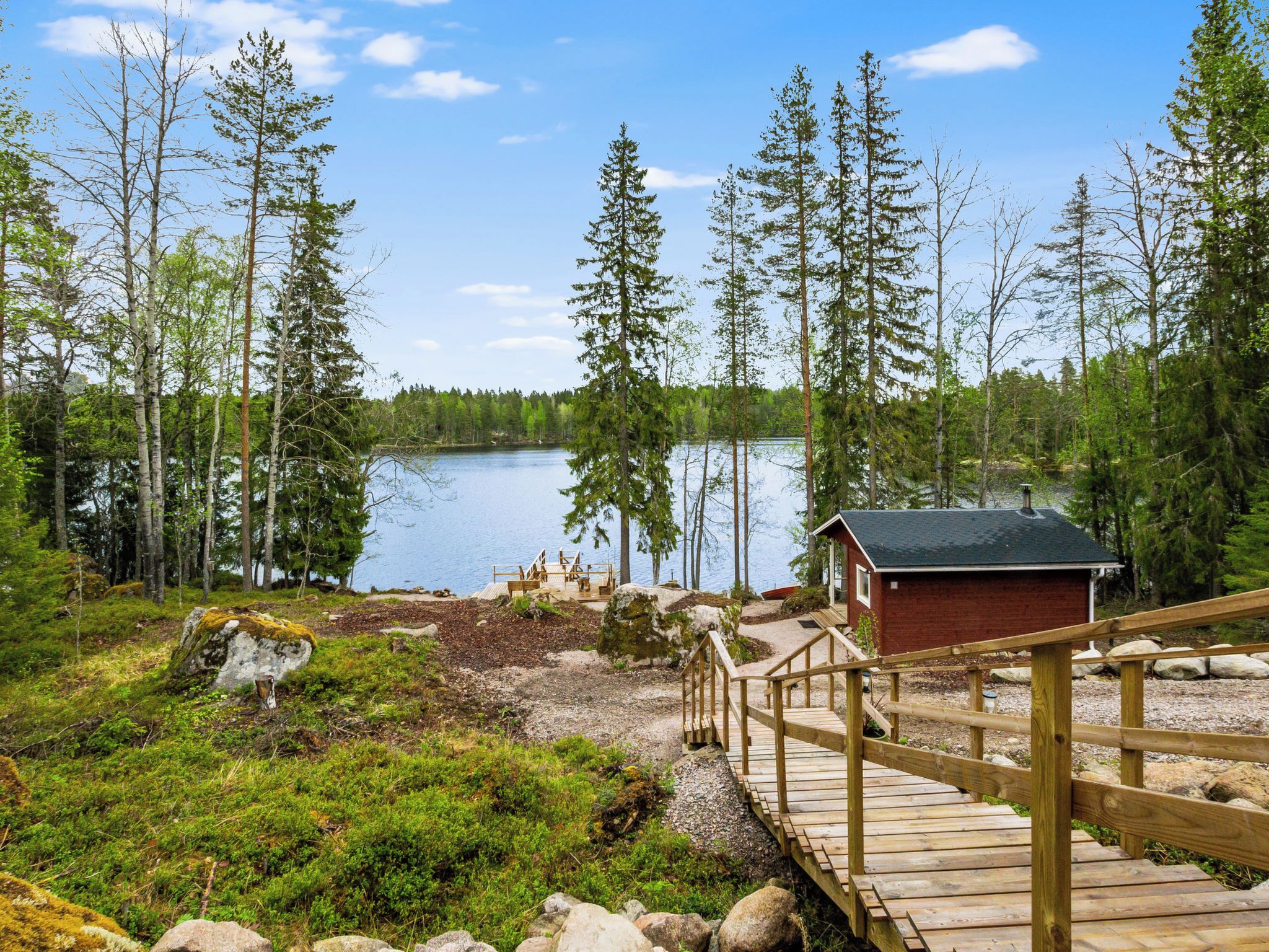 Eine Holzterrasse führt zu einer Hütte am See, umgeben von Bäumen.