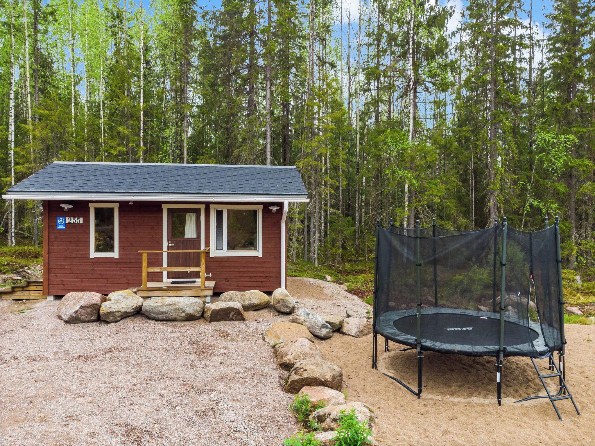 Une petite cabane portant le numéro 255, un trampoline et une terrasse en bois.