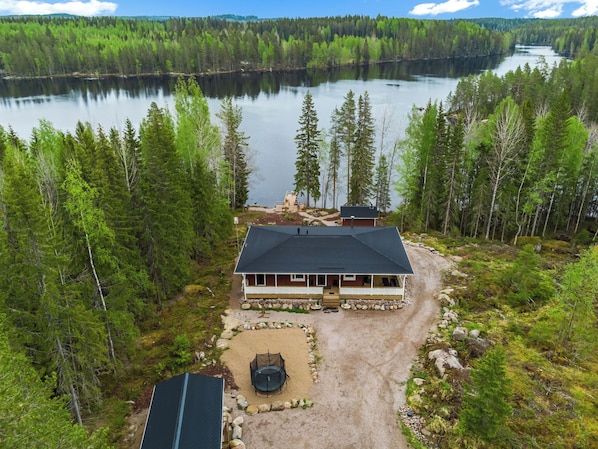 A cabin with a large deck, a fire pit, and a view of a lake surrounded by forest.
