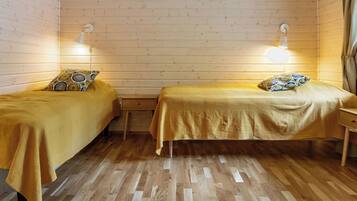A room with two single beds, wooden flooring, and wall-mounted lamps.