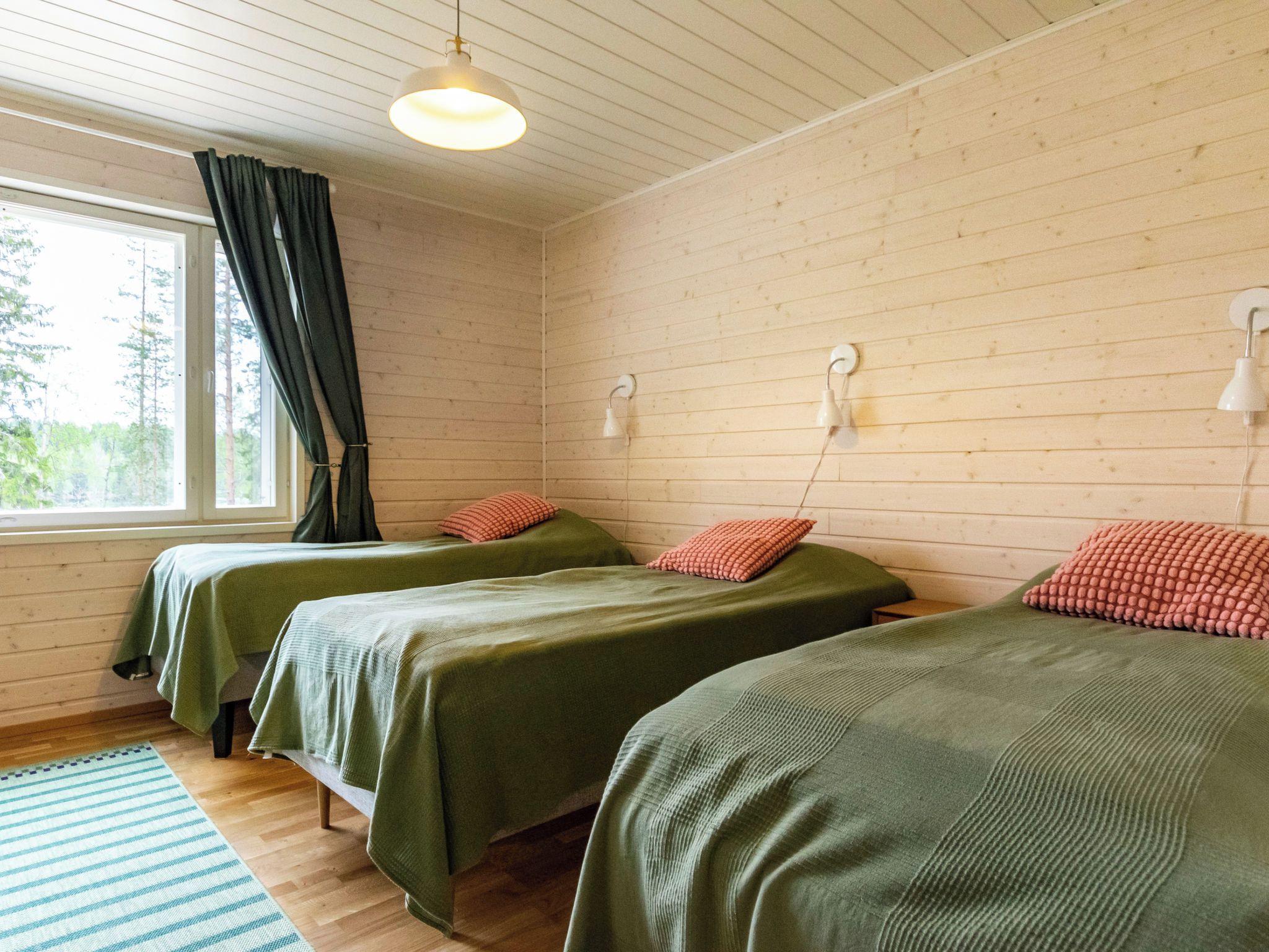 Ein Zimmer mit zwei Betten, einem Vorhangfenster, Holzboden und einer Pendelleuchte.