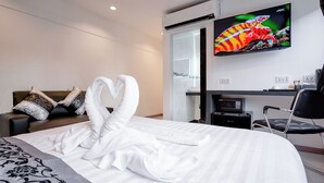 Camera d'albergo con un letto grande, una TV a schermo piatto montata a parete, una scrivania con sedia e un divano con cuscini decorativi.