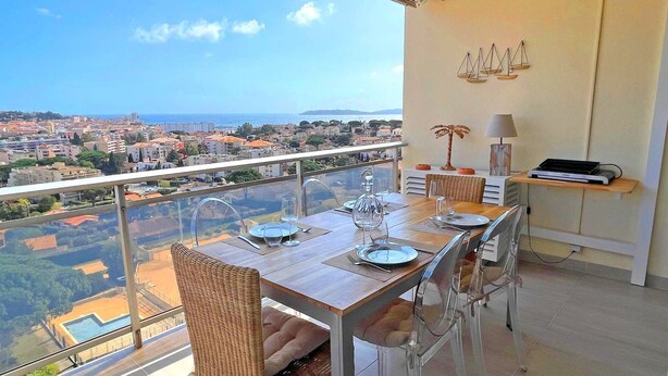 A dining area with a table set for four, overlooking a cityscape and the sea.
