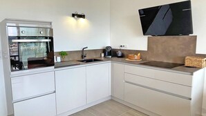 A modern kitchen with a built-in oven, a sink, a coffee maker, and a flat-screen TV mounted on the wall.