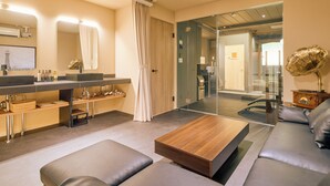 Una habitación de hotel moderna con un espejo grande, una mesita de centro de madera, un sofá y un baño con tocador.