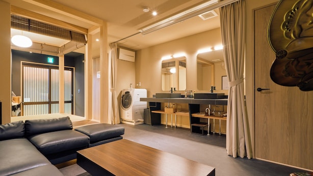 Una habitación de hotel moderna con sofá, una mesa de centro de madera, lavadora, lavabo y un espejo grande.