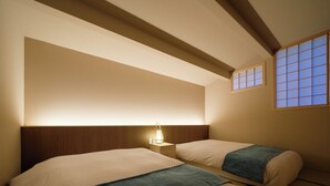 Habitación de hotel con dos camas, una mesita de noche con lámpara y una ventana con puertas correderas de papel.