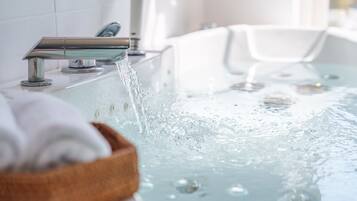 A bathtub with running water, a wooden bath mat, and a modern faucet.