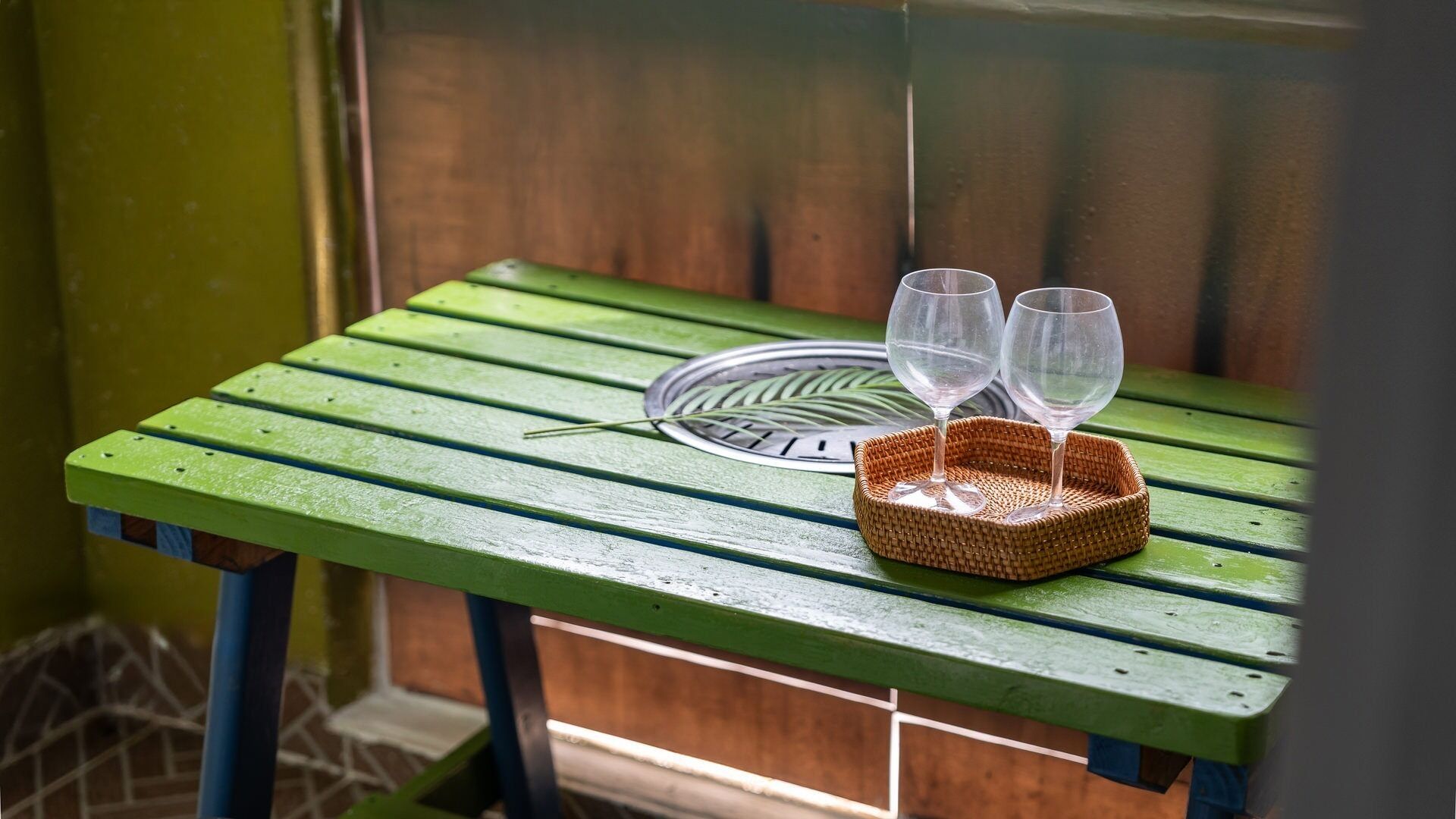 A green wooden table with two wine glasses and a tray.