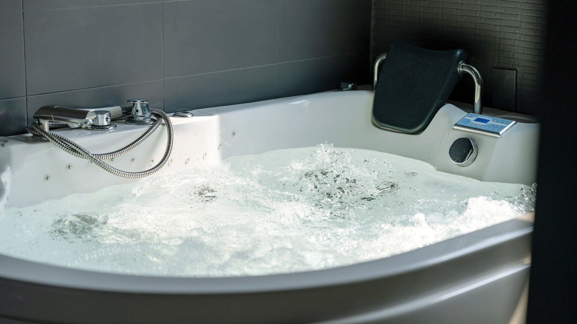 A bathtub with running water, a handheld showerhead, and a control panel.