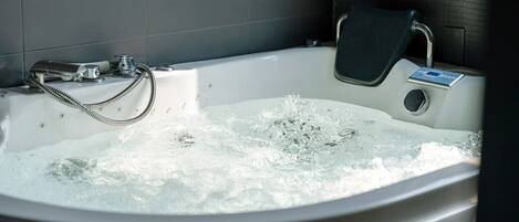 A bathtub with running water, a handheld showerhead, and a control panel.