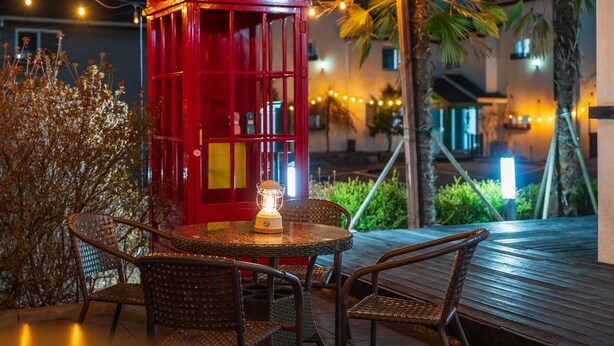 An outdoor seating area with wicker chairs and a table, a red lantern, and string lights. - Gyeongju The Stay Spa Pension (Gyeongju)