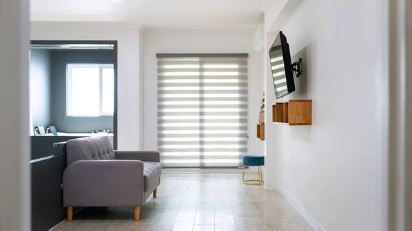 Una sala de estar moderna con un sofá gris, un televisor montado en la pared y un ventanal corredero que da a un balcón.