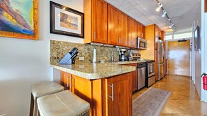 A kitchen with wooden cabinets, granite countertops, stainless steel appliances, and a bar stool.