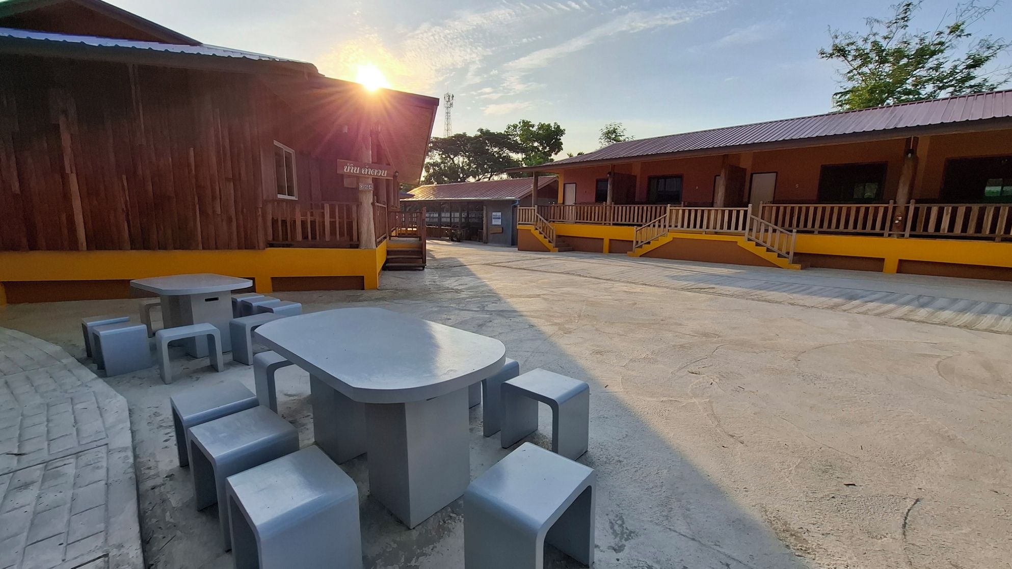 An outdoor seating area with tables and benches, a wooden building with a sign, and a yellow-roofed structure with a staircase.
