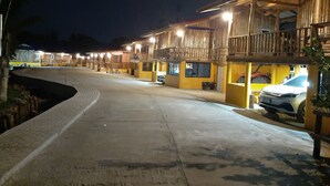 Un hilera de edificios de madera con balcones, un sendero pavimentado y coches aparcados.