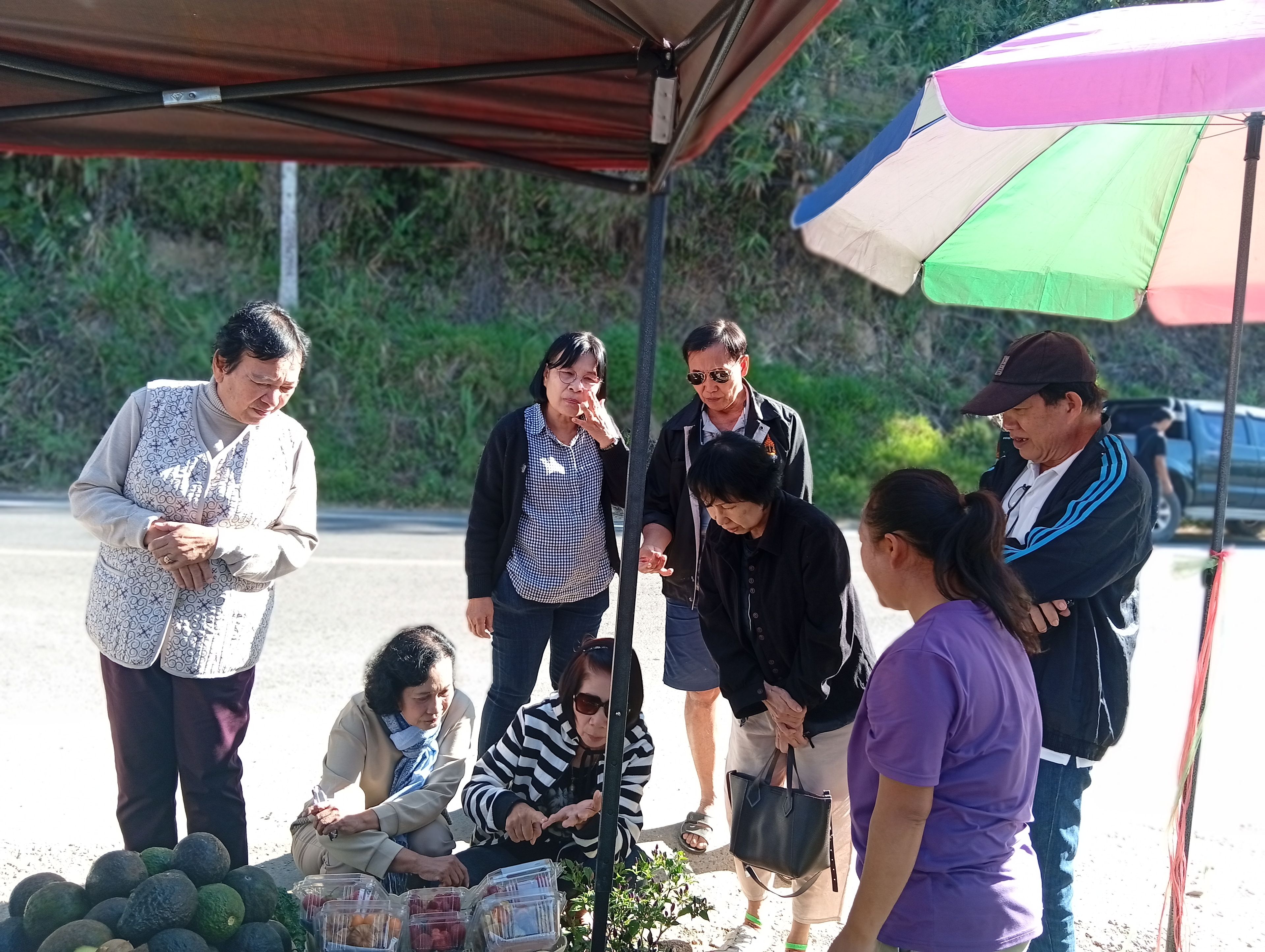 Un groupe de personnes s’est rassemblé autour d’un étal de fruits placé sous une tente.