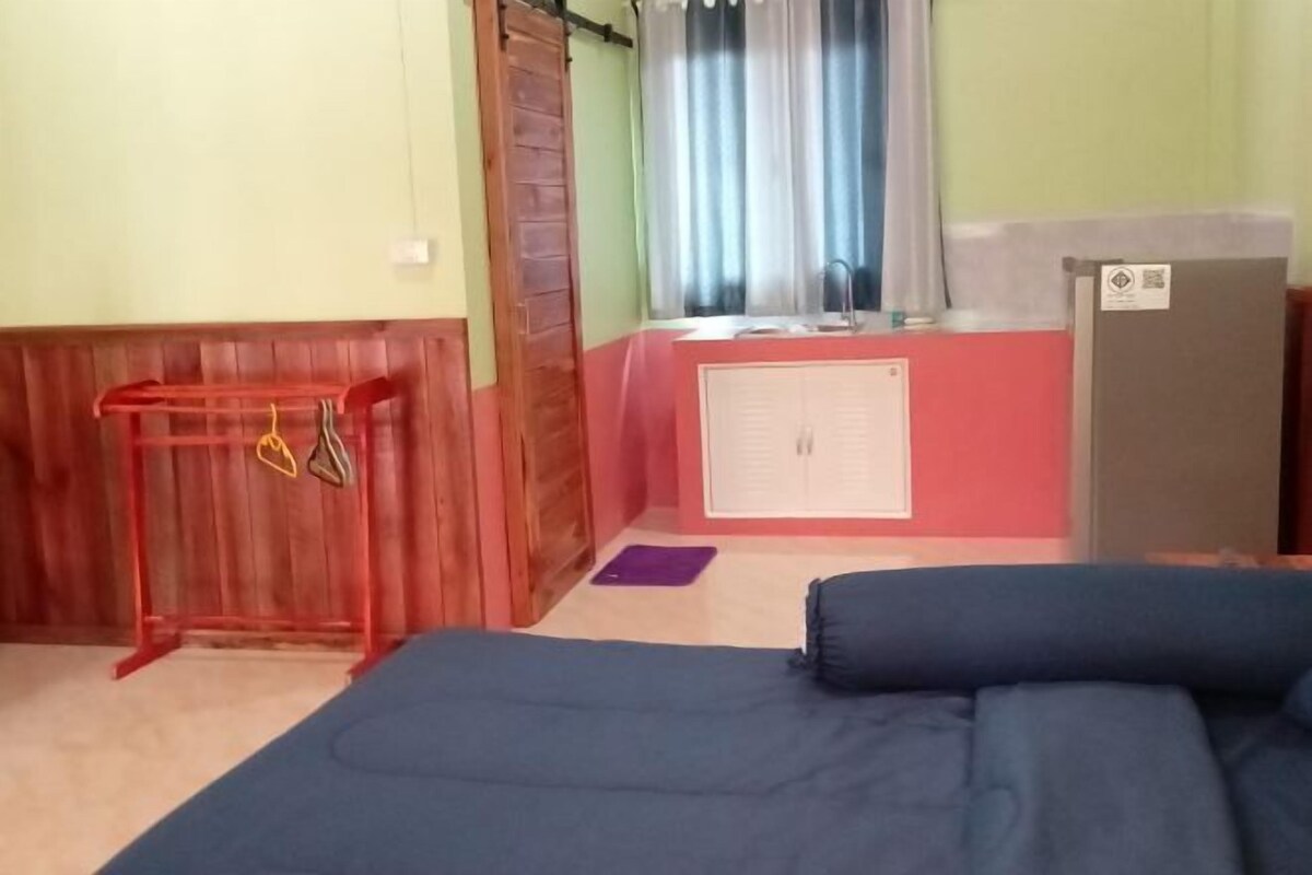 Un dormitorio con cama, una mesita con objetos colgando, un armario, una ventana con cortinas y un radiador.