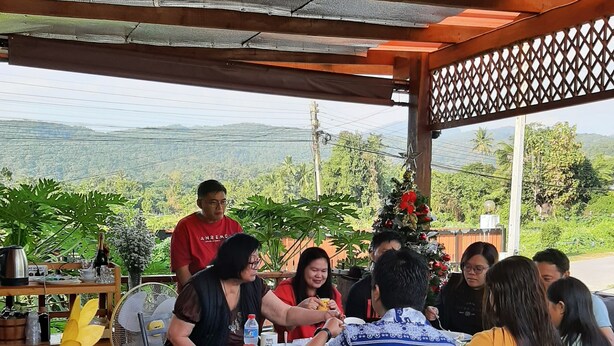 Un grupo de personas cenando en una mesa de madera al aire libre, con vistas a las colinas.