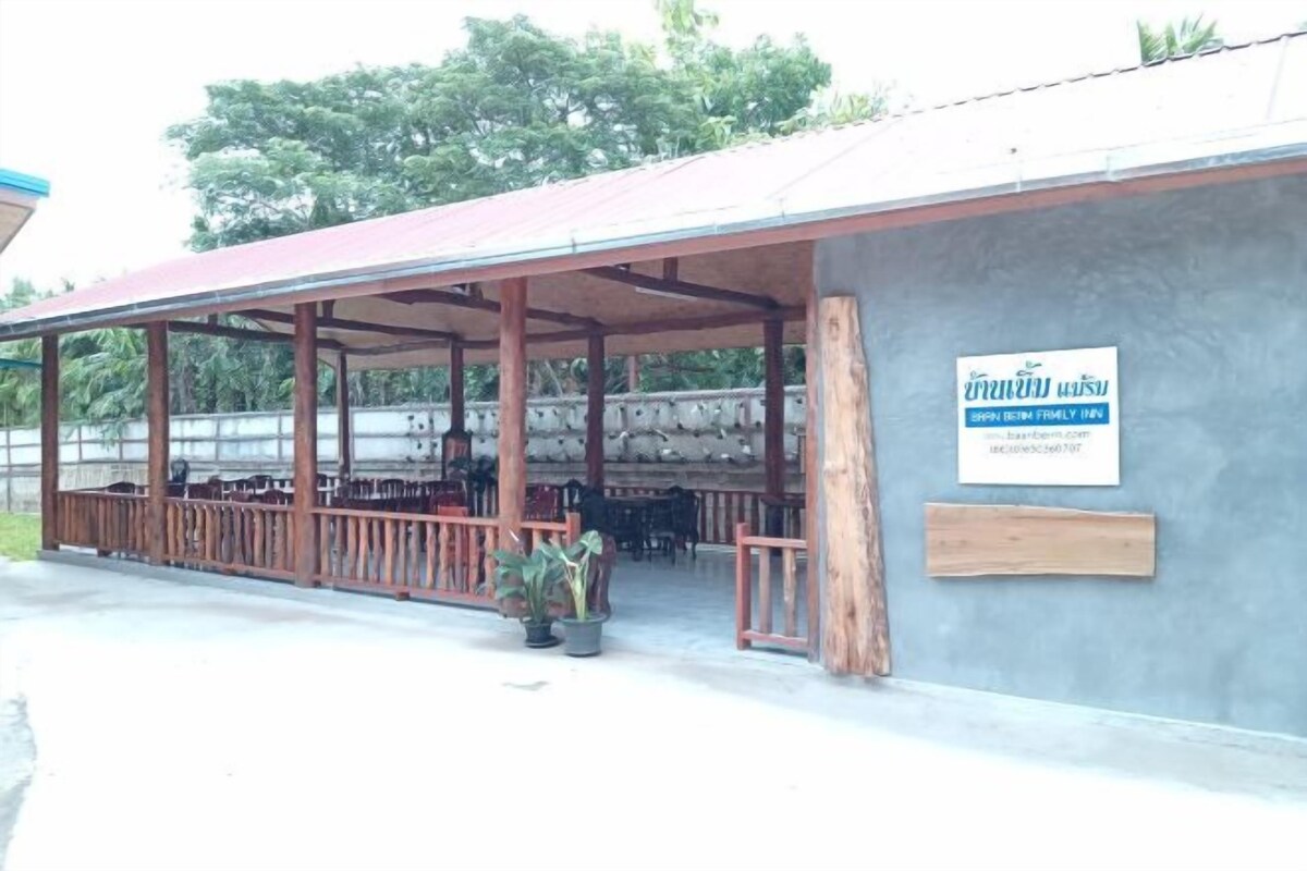 Un espacio al aire libre cubierto con bancos de madera y plantas en macetas, un letrero para Shan Beit Family Inn y un muro de concreto.