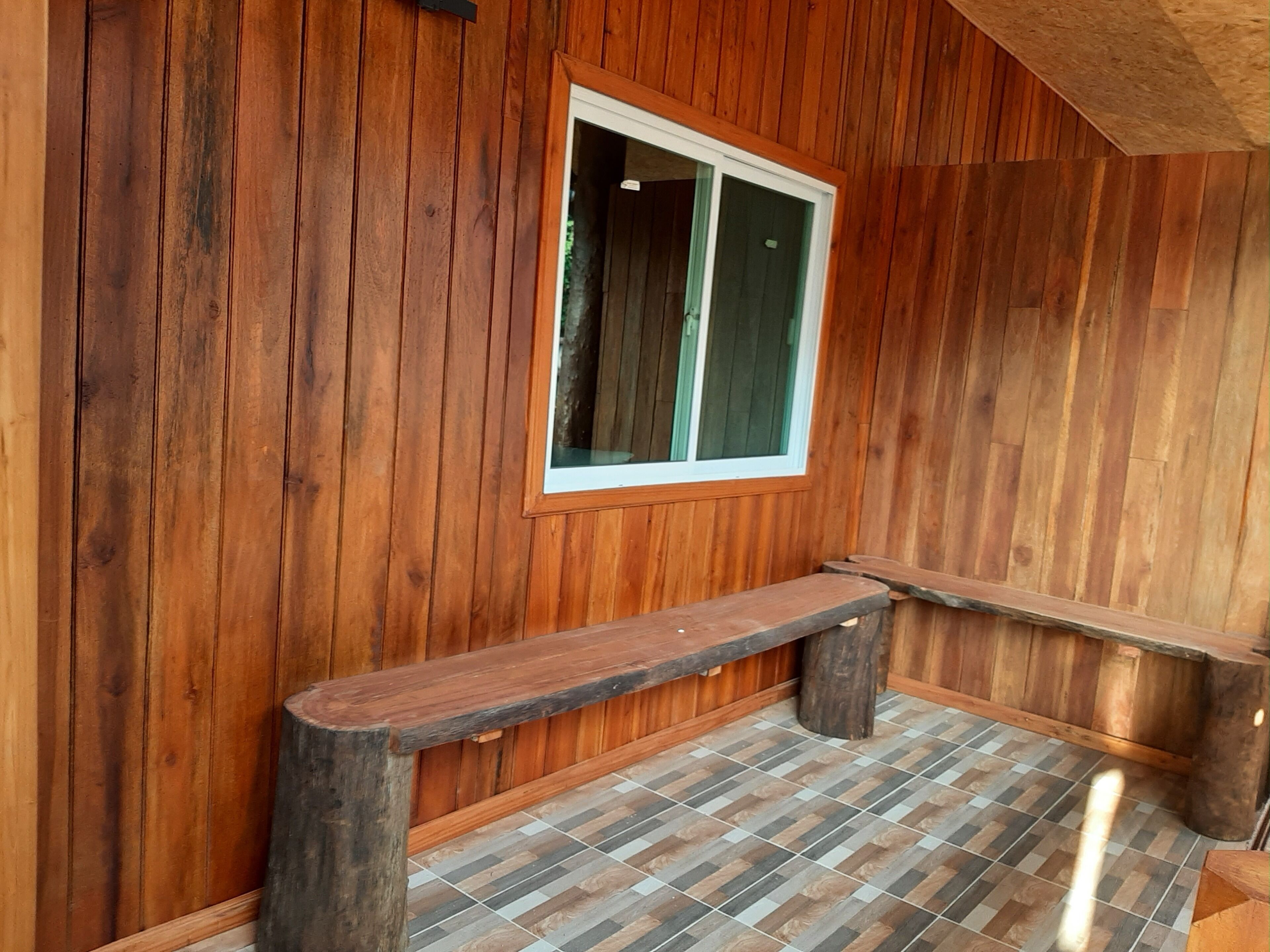 A wooden interior with a bench, a window, and a tiled floor.