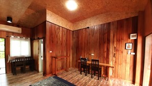 Una habitación con paredes de madera, una cama con colchón azul, una mesa de madera con sillas y una ventana con cortinas.