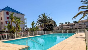 A swimming pool with a tiled deck, surrounded by a white fence and palm trees. - Studio cabine 4 personnes,copropriété avec  Piscine (LE LAVANDOU)