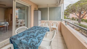 A balcony with a table and chairs, a sliding glass door, and a view of the street and trees. - Studio cabine 4 personnes,copropriété avec  Piscine (LE LAVANDOU)