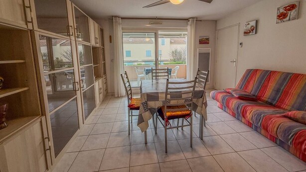 A dining area with a table and chairs, a ceiling fan, and a colorful sofa. - Studio cabine 4 personnes,copropriété avec  Piscine (LE LAVANDOU)