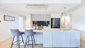 Une cuisine moderne dotée d’un grand îlot central, de deux tabourets de bar, d’un réfrigérateur en acier inoxydable et d’une carte du monde accrochée au mur.