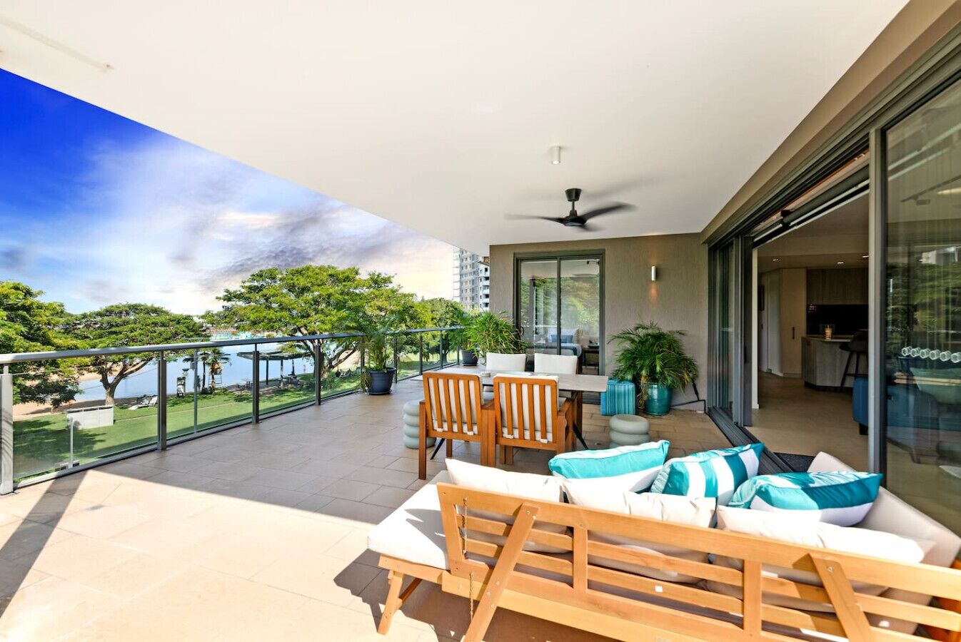 A balcony with a table and chairs, potted plants, and a view of a body of water and trees.