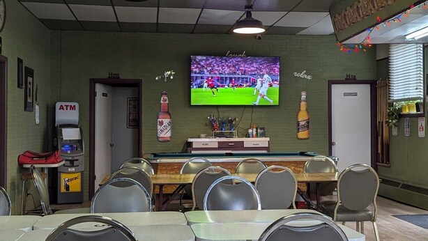 A bar area with a television displaying a sports event, a cash register, and a bottle of Canadian beer on the wall. - Dinsmore Hotel (Dinsmore)