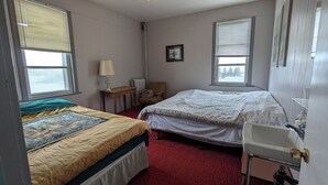 A bedroom with two beds, a small table with a lamp, a chair, and a window. - Dinsmore Hotel (Dinsmore)