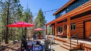 A wooden cabin with a covered patio area featuring outdoor seating and red umbrellas.