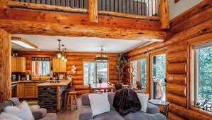 A log cabin interior with a dining area, kitchen, and living room.