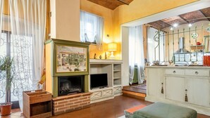 A living room with a fireplace, television, and a kitchen area with cabinets and a stove. - GuestHost - San Rocco Apartment Borgo a Mozzano - Lucca (Borgo a Mozzano)