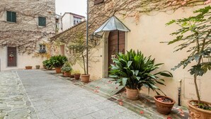 A narrow cobblestone street with potted plants and a building with a wooden door. - GuestHost - San Rocco Apartment Borgo a Mozzano - Lucca (Borgo a Mozzano)