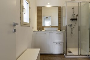 A bathroom with a sink, mirror, cabinets, and a glass-enclosed shower.