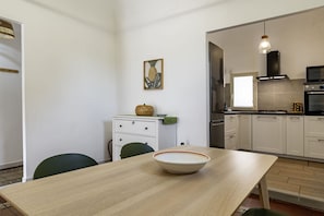 Moderni keittiö, jossa on valkoiset kaapit, ruokapöytä ja sen päällä kulho sekä vihreä tuoli.