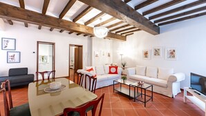 A living room with a wooden ceiling, a white sofa, a dining table with chairs, and a TV on a stand. - GuestHost - Large Apartment in the Historic Center of Parma (Parma)