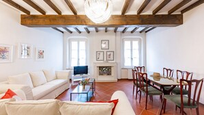 A living room with a sofa, TV, fireplace, dining table, and chairs. - GuestHost - Large Apartment in the Historic Center of Parma (Parma)