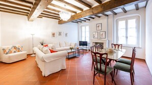A spacious living area with a fireplace, white sofas, a dining table with chairs, and exposed wooden beams. - GuestHost - Large Apartment in the Historic Center of Parma (Parma)