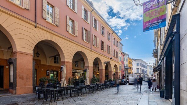 A cobblestone street with outdoor seating, a café, and a building with arches. - GuestHost - Large Apartment in the Historic Center of Parma (Parma)