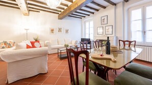 A well-lit living room with a high ceiling, wooden beams, a dining table with chairs, a sofa, and a TV. - GuestHost - Large Apartment in the Historic Center of Parma (Parma)