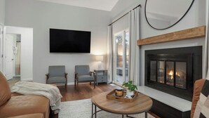 Een woonkamer met een open haard, twee fauteuils, een bank, een flatscreen televisie en een salontafel met een dienblad.