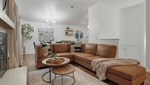 Een moderne woonkamer met een bruine leren hoekbank, een ronde salontafel en een kroonluchter.