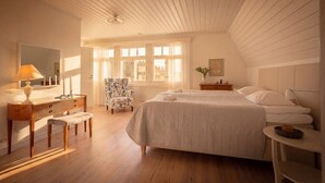 Un dormitorio con una cama grande, un escritorio con lámpara, una silla y una ventana con cortinas.