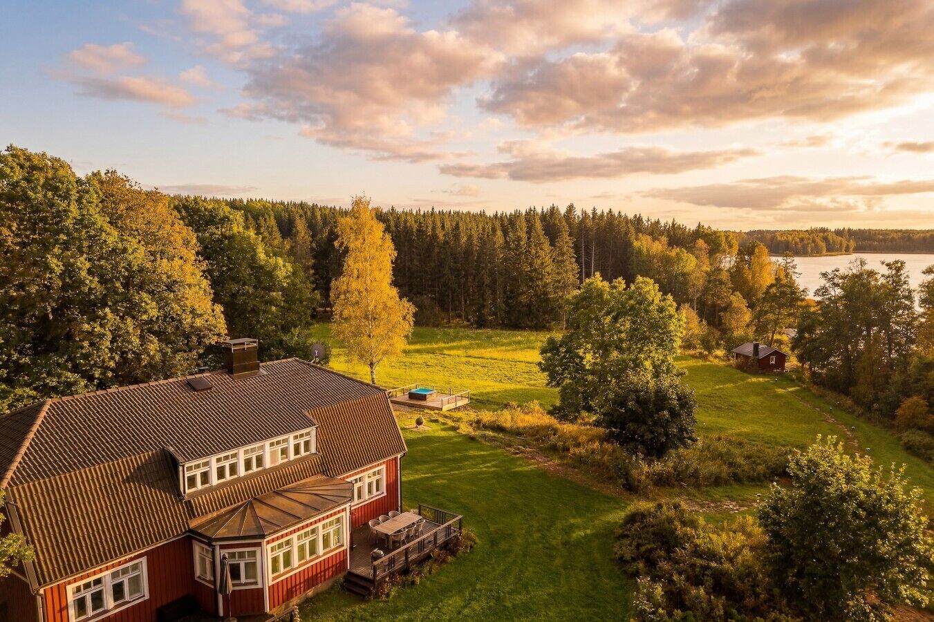 Ein großes Haus mit roter Fassade, einer Terrasse und Blick auf See und Wald.