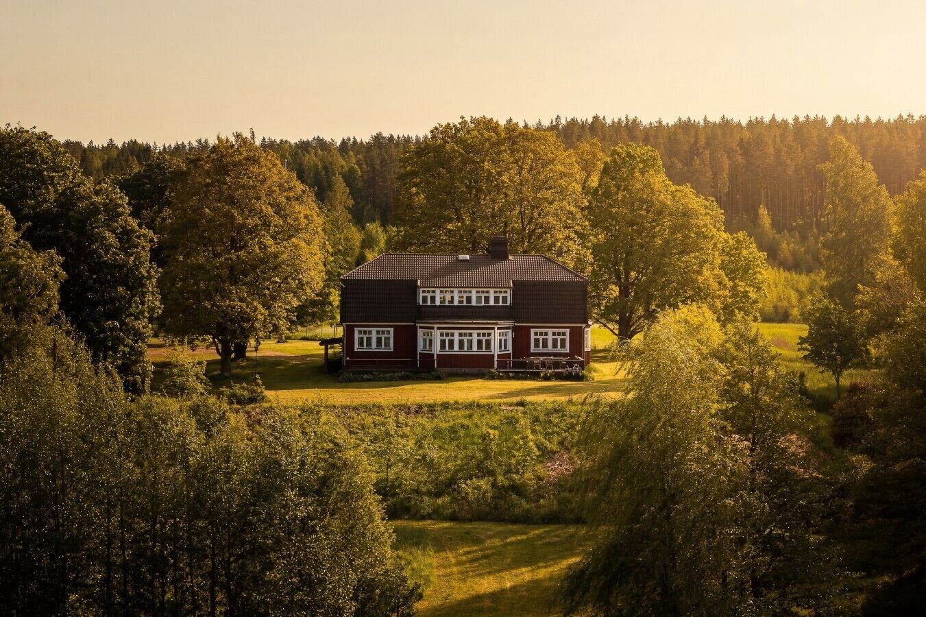 Et toetagers hus med mørkt tag og hvidt pynt, omgivet af frodig vegetation og træer.
